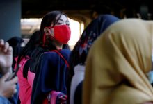Woman wearing protective mask looks on as she waits for a commuter train at a station in Jakarta