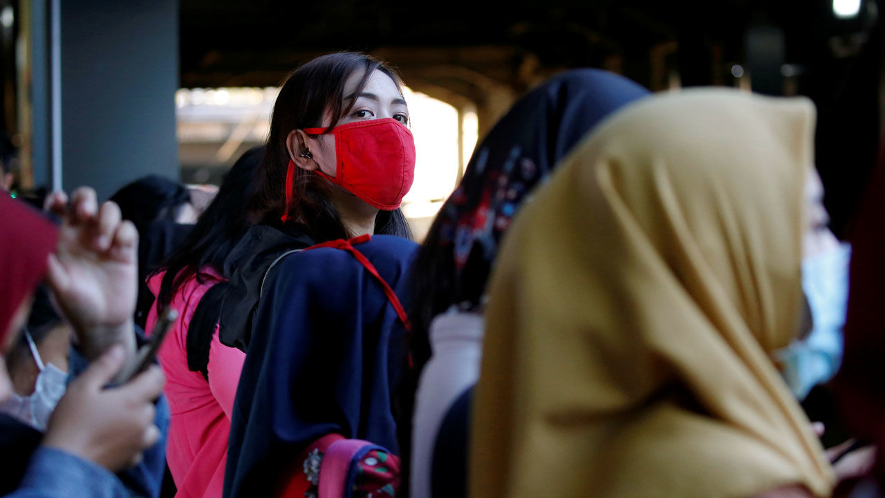 Woman wearing protective mask looks on as she waits for a commuter train at a station in Jakarta